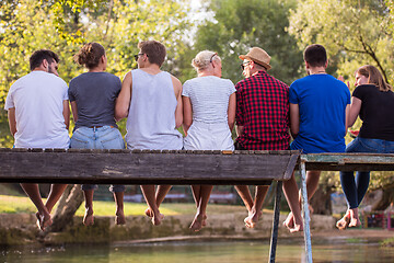 Image showing rear view of friends enjoying watermelon while sitting on the wo