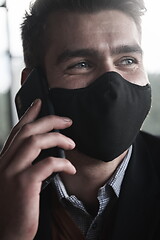 Image showing business man wearing coronavirus medical face mask while using smartphone