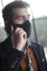 Image showing business man wearing coronavirus medical face mask while using smartphone