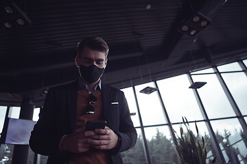 Image showing business man wearing coronavirus medical face mask while using smartphone