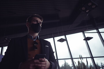 Image showing business man wearing coronavirus medical face mask while using smartphone