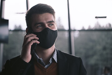 Image showing business man wearing coronavirus medical face mask while using smartphone