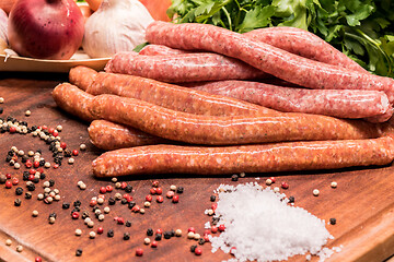 Image showing raw sausages with chilli and herbs on a wooden board with spices