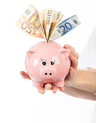 Image showing A woman shows a piggy bank full of European banknotes