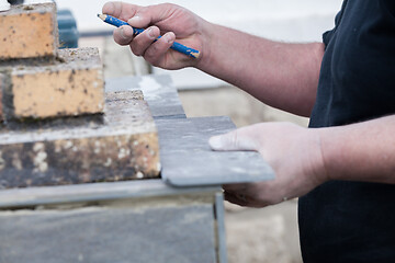 Image showing the tiler measures and puts marks to cut and lay a tile