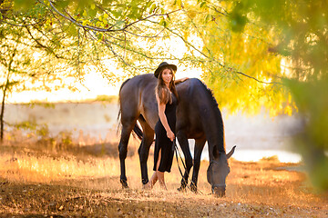 Image showing Girl walks in the forest with a horse at sunset