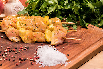 Image showing raw chicken skewers marinated with lemon on a wooden board
