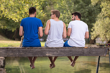 Image showing men enjoying watermelon while sitting on the wooden bridge