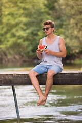 Image showing man enjoying watermelon while sitting on the wooden bridge