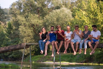 Image showing friends enjoying watermelon while sitting on the wooden bridge