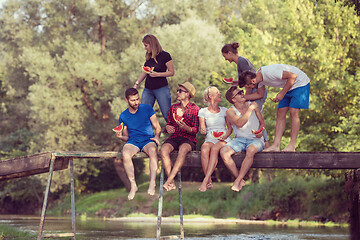 Image showing friends enjoying watermelon while sitting on the wooden bridge