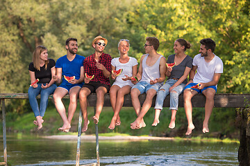 Image showing friends enjoying watermelon while sitting on the wooden bridge