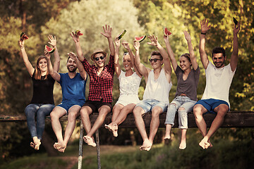 Image showing friends enjoying watermelon while sitting on the wooden bridge