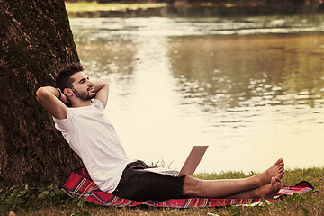 Image showing man using a laptop computer on the bank of the river