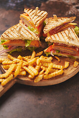 Image showing Club sandwiches served on a wooden board. With hot French fries