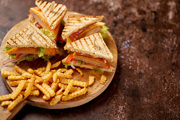 Image showing Chicken and cheese club sandwiches served on a wooden board with french fries