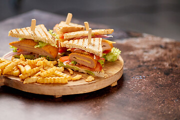 Image showing Chicken and cheese club sandwiches served on a wooden board with french fries