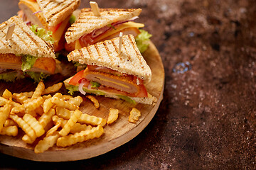 Image showing Club sandwiches served on a wooden board. With hot French fries