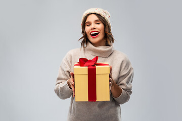 Image showing young woman in knitted winter hat holding gift box