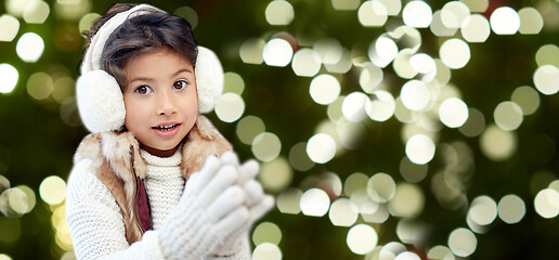 Image showing happy little girl in earmuffs over winter forest