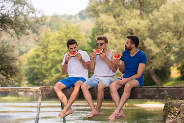 Image showing men enjoying watermelon while sitting on the wooden bridge