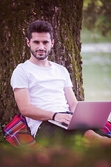 Image showing man using a laptop computer on the bank of the river