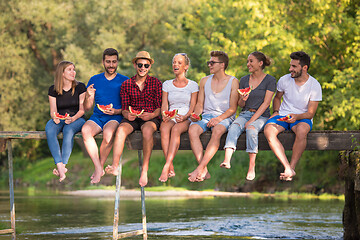 Image showing friends enjoying watermelon while sitting on the wooden bridge