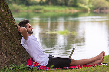 Image showing man using a laptop computer on the bank of the river