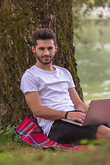 Image showing man using a laptop computer on the bank of the river