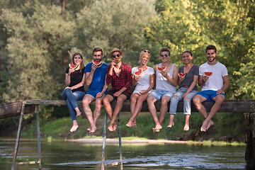 Image showing friends enjoying watermelon while sitting on the wooden bridge