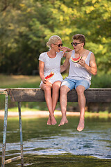 Image showing couple enjoying watermelon while sitting on the wooden bridge