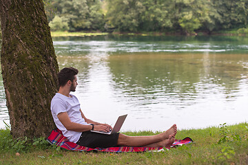 Image showing man using a laptop computer on the bank of the river