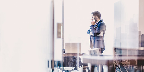 Image showing Businessman talking on a mobile phone in corporate office while looking through window.