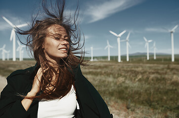 Image showing Woman with long tousled hair next to the wind turbine with the w