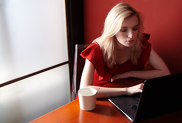 Image showing Young adult woman wearing red jumpsuit and using laptop