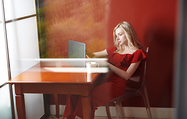 Image showing Young adult woman sitting at the table and working on laptop