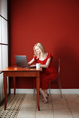 Image showing Young adult woman sitting at the table and working on laptop