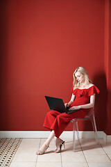 Image showing Young adult woman sitting on a chair and working on laptop