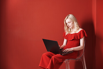 Image showing Young adult woman sitting on a chair and working on laptop