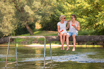 Image showing couple enjoying watermelon while sitting on the wooden bridge