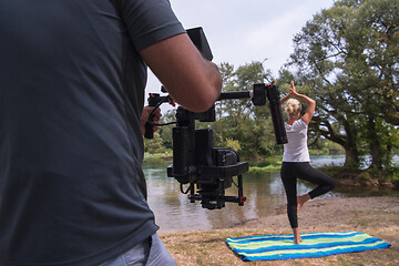 Image showing young videographer recording while woman doing yoga exercise