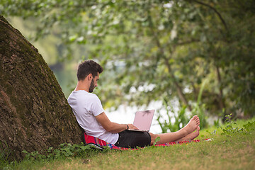 Image showing man using a laptop computer on the bank of the river