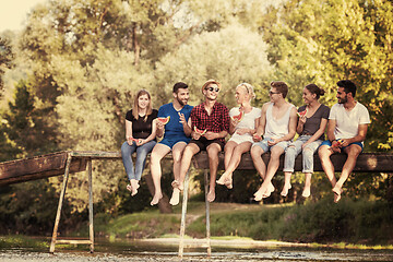 Image showing friends enjoying watermelon while sitting on the wooden bridge