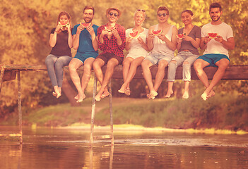 Image showing friends enjoying watermelon while sitting on the wooden bridge