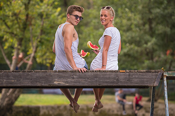 Image showing couple enjoying watermelon while sitting on the wooden bridge