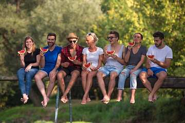 Image showing friends enjoying watermelon while sitting on the wooden bridge