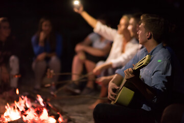 Image showing young friends relaxing around campfire