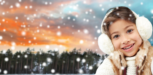 Image showing happy little girl in earmuffs over winter forest