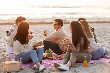 Image showing happy friends eating sandwiches at picnic on beach