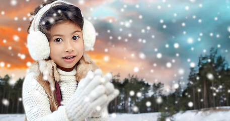 Image showing happy little girl in earmuffs over winter forest